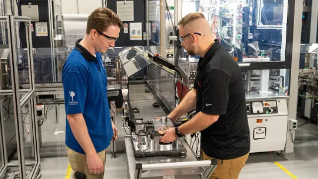 Two staff members working with equipment in a manufacturing facility.