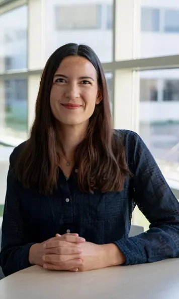 Portrait of a person seated at a table in a bright office.