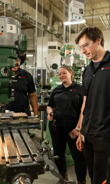 Three staff members gathered around machinery in a workshop.