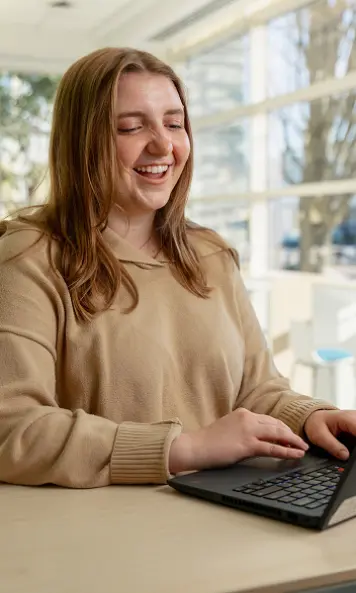 Person working on a laptop at a desk in a bright indoor space.