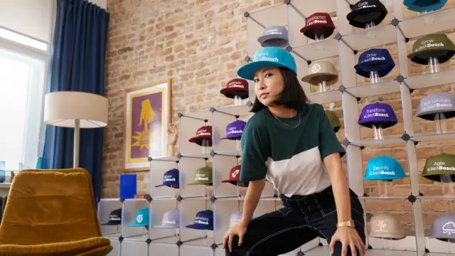 Person wearing cap poses in room with wall display of colorful caps arranged on shelves