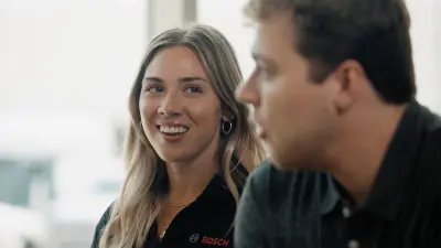 Two people sit at a table talking; “Bosch” is visible on clothing.