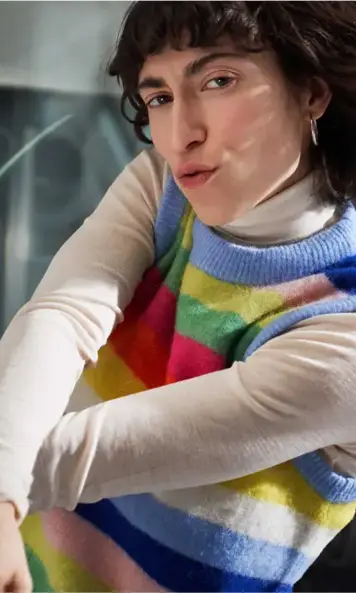 Close-up of person wearing colorful striped sweater and light turtleneck, leaning forward near window light
