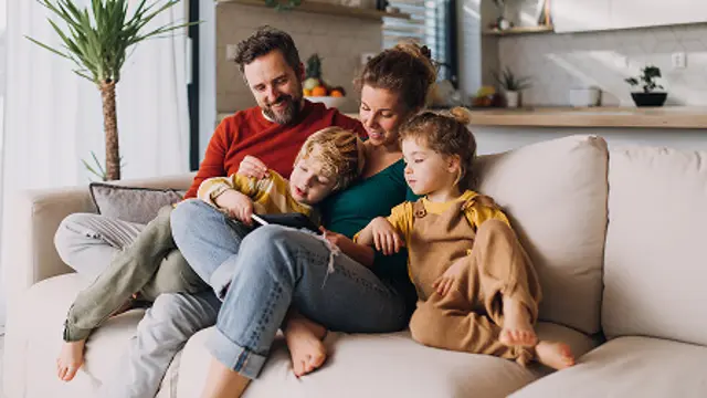 Four people sitting closely together on a sofa at home.