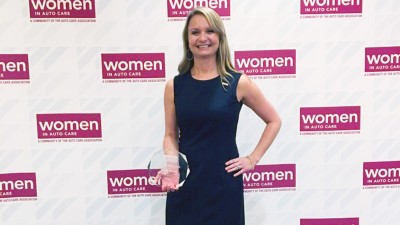 Nicole Huard standing in front of a Women in Auto Care award poster.